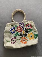 Front view of beige handbag with colorful embroidered flowers and round beige handles.