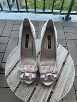 Pair of silver satin peaked toe high heels shown from above on wooden table outdoors, showing overall condition.