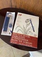 Photo of spiral-bound sketchbook and pack of 3 Koh-I-Noor My First Norica HB pencils with sharpener on wooden surface