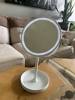 Front view of white magnifying mirror, showing circular design with LED light ring and round tray base.