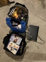Overview photo showing the three reusable bags full of DVDs alongside the Sony DVD player and remote on a concrete floor.