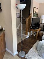 Full view of the tall floor lamp showing its slender silver base and white glass shade in a living room setting.