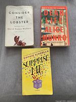 Photo showing all three paperback books together on gray surface: 'Consider The Lobster', 'Dear Life', and 'Surprise Me'.