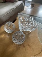 Full view of all three crystal pieces on wooden table showing square bowl and two round lidded vessels