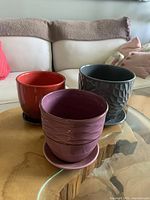 Three ceramic plant pots arranged on glass coffee table showing colors and styles: deep orange, mauve, and dark grey with textured pattern.