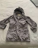 Full view of the grey women's jacket laid flat showing hood, zip front and pockets.