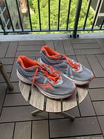 Side angled view of the gray and orange women's running shoes on a small round wooden table on balcony with city background