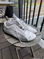 Side and angled view of white and gray Puma sneakers on round wooden table showing minimal creasing and clean soles.
