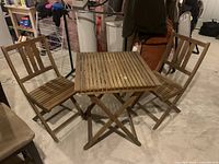 Photo showing full patio furniture set with two wooden folding chairs and one folding table displaying the collapsable features and slatted design.