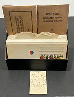 Top view of the box filled with cardboard eye test training cards showing colorful illustrations, and a separate small card with perforated holes pattern at the front.
