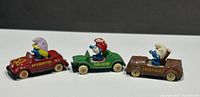 Three ERTL Smurf diecast cars in red, green, and brown with Smurfette, Papa Smurf, and Smurf character figures seated inside, visible wear on paint and details.