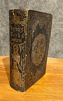 Spine view showing gold embossed title, decorative portrait and floral designs on dark leather cover.