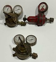 Three antique brass and one red metal pressure gauges with dials, adjustment levers, and connectors arranged on white background.