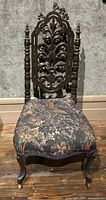 Front view of antique carved wood side chair with upholstered floral fabric seat and ornate carved backrest.