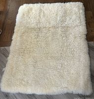 Full view of a creamy white lambskin wool mattress topper laid on a wooden floor.