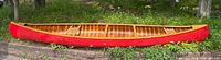 Full side profile of canoe showing red exterior and wood interior rim.