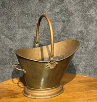Front angled view of the large brass coal scuttle showing the helmet shape, arched handle, spout, and round base.