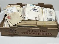 Box filled with assorted first day covers and covers in various conditions with postage stamps and cancellations.