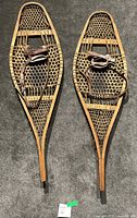 Pair of antique wooden snowshoes laid flat, showing full length and width with leather bindings