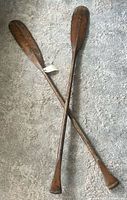 Pair of crossed wooden canoe paddles laid on textured carpet showing full length and general wear