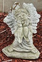 Front view of weathered concrete angel statue showing chips on wings and weathered surface.