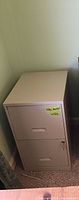 Closed 2-drawer metal filing cabinet showing taupe color and working lock with key inserted.