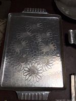 Photo of rectangular aluminum tray featuring embossed daisy flower pattern, showing the surface and handles