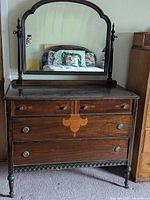 Front view of antique dark wood vanity dresser with mirror reflecting bed and room.