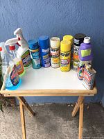 Photo of assorted cleaning sprays and aerosol cans on a folding wooden tray against a blue wall