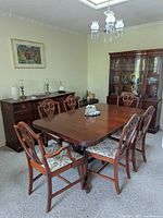 Full view of the rectangular mahogany dining table with six matching chairs with floral upholstered seats. Behind the table is a mahogany sideboard and a glass-fronted china cabinet.