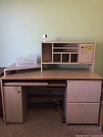 Front view of light wood computer desk with upper shelving and plastic organizer on the left side of desk surface.