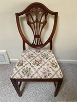 Front view of the wooden dining chair with floral fabric seat, showing carved shield-shaped backrest with fan motif