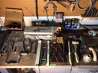 Full view of woodworker's bench with various hand tools and hardware items arranged, showing saws, pliers, brushes, crowbars, hammers, and boxed hardware.