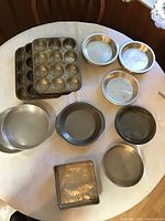 Photo showing all aluminum pans arranged on table including cupcake pans, pie pans, cake pans and steamers