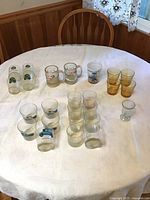 Photo of numerous vintage glassware and mugs arranged on round table showing A&W, Velvet Turtle mugs, amber glasses and clear glasses