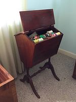Wooden cradle with open hinged top showing multiple spools of colorful thread inside.