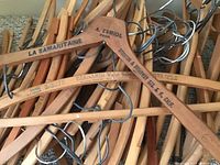 Close-up of several vintage wooden hangers showing metal hooks and printed brand/store names on wood.