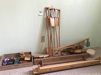 Various handcrafted wooden items displayed on carpet including paddles, wooden base with arm, and multiple wooden toys and decorative items in a box