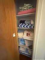 View of folded blankets, quilts, towels, and travel pillow stacked in shelving unit