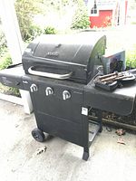 Full frontal view of the Char-Broil propane BBQ grill showing 3 control knobs, side shelves and grill utensils on the right shelf.