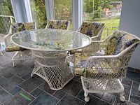 Five-piece white woven patio set with glass table and four chairs on tiled floor