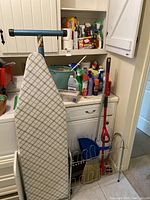 Ironing board, shoe rack with broom and mop, various cleaning supplies on shelves