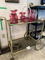 Full view of the brass and smoked glass tea/cocktail cart with the pink pressed glass items on the top shelf.