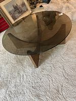 Angled view showing the smoke-tinted round glass top and the wooden base with intersecting curved panels forming a cross design.