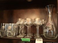 Shelf display showing the set of glassware: one decanter, four stemmed wine glasses, and four water glasses, all with pink floral designs.