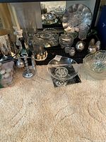 Shows a comprehensive view of the lot items arranged on a black wire shelf and carpet, including glass bowls, metal plates, candles, and decorative figurines