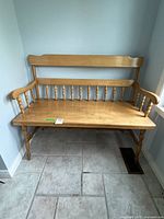 Full view of the early wooden bench showing its backrest with horizontal slats and vertical spindles, armrests, and legs.