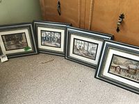 Four framed art prints arranged on the floor leaning against cabinetry, showing overall set and frame style.