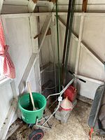 Gardening tools in a shed including a green bucket, metal garden cage, garden aerator, and rake.