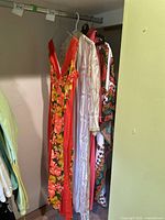 Photo showing a red floral dress, white embroidered dress, and multicolor patterned dress hanging on a closet rod.